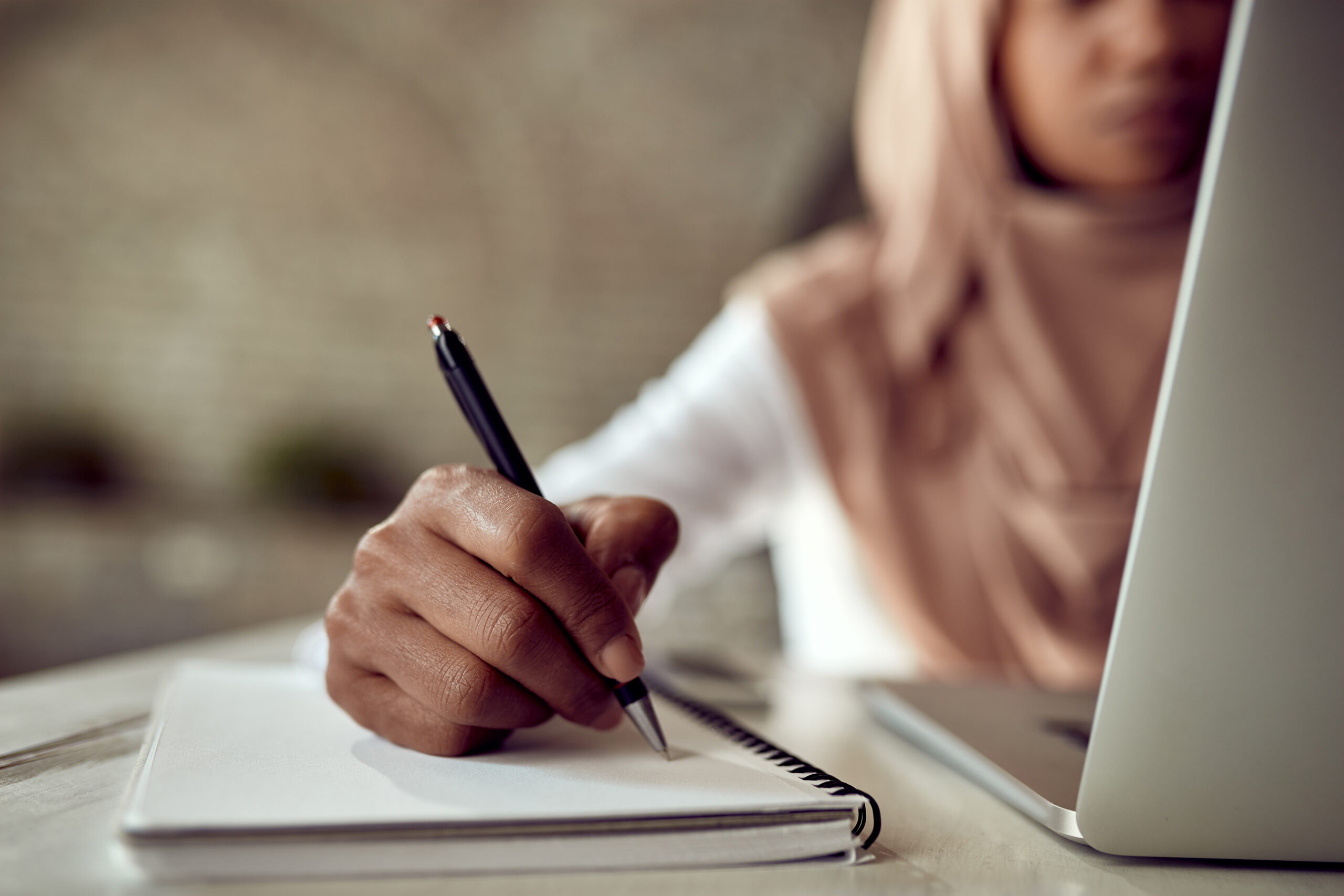 closeup black muslim businesswoman writing notes while working computer office scaled
