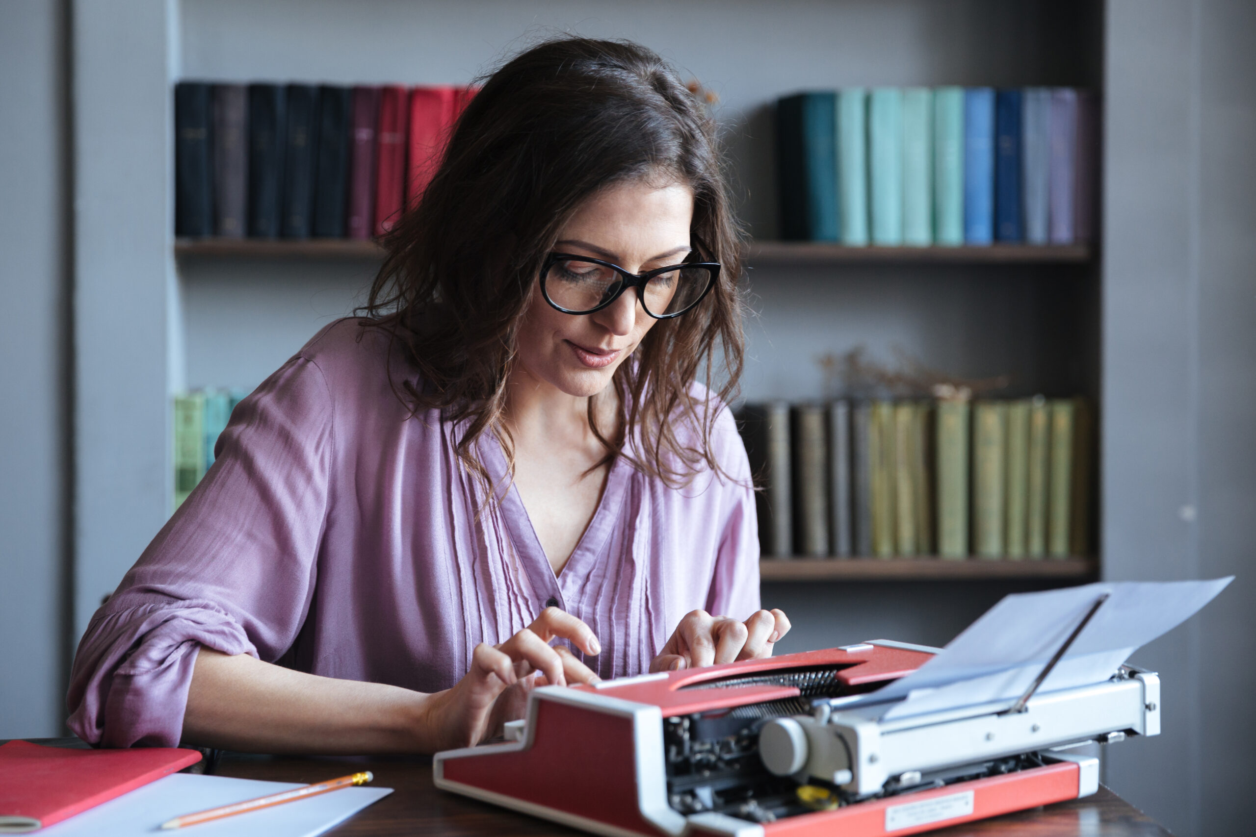 brunette mature woman journalist eyeglasses typing typewriter indoors scaled